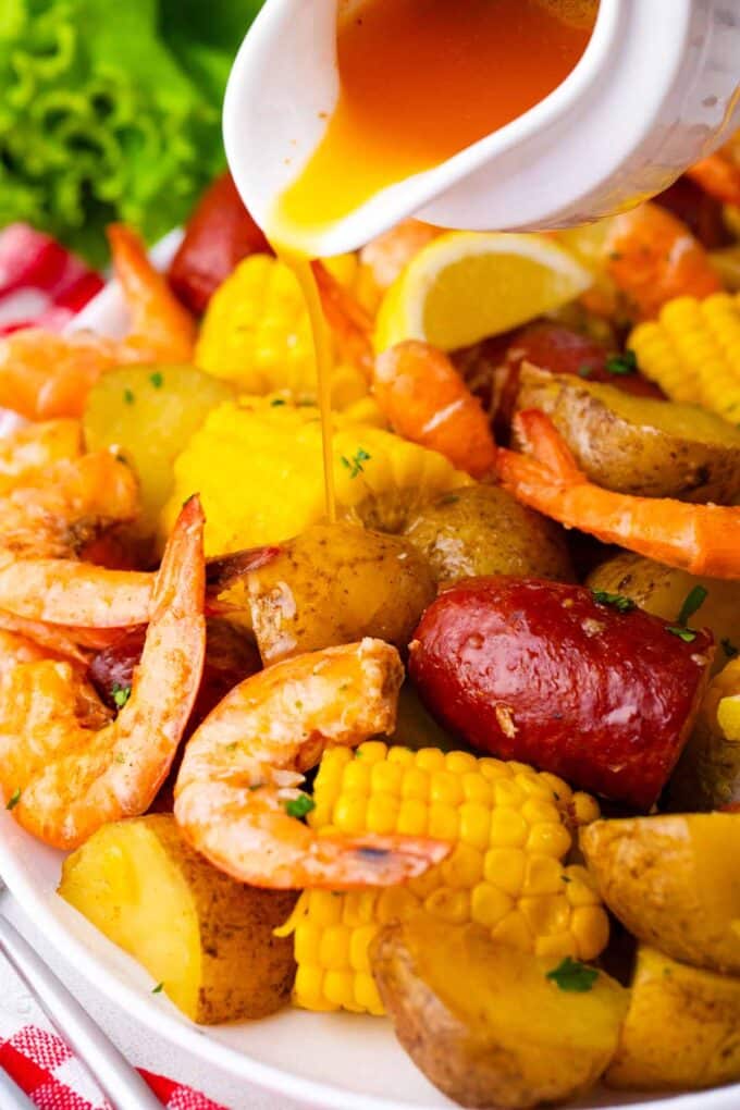 Pouring seasoned melted butter on top of instant pot shrimp boil on a plate.