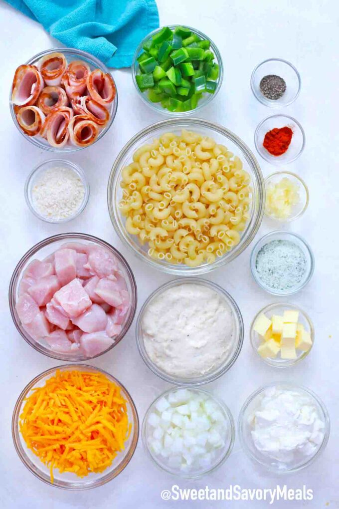 pasta bacon raw chicken cheese and other ingredients to make chicken casserole, arranged in bowls on a table