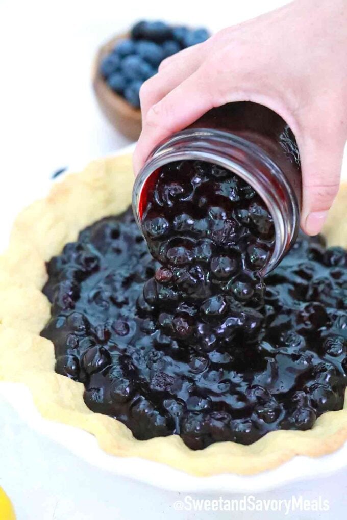 adding blueberry pie filling to a pie crust