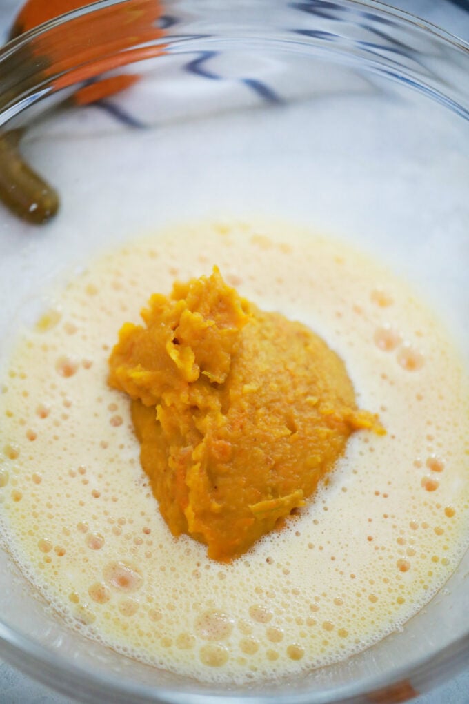 Adding pumpkin puree to pumpkin roll mix in a bowl.