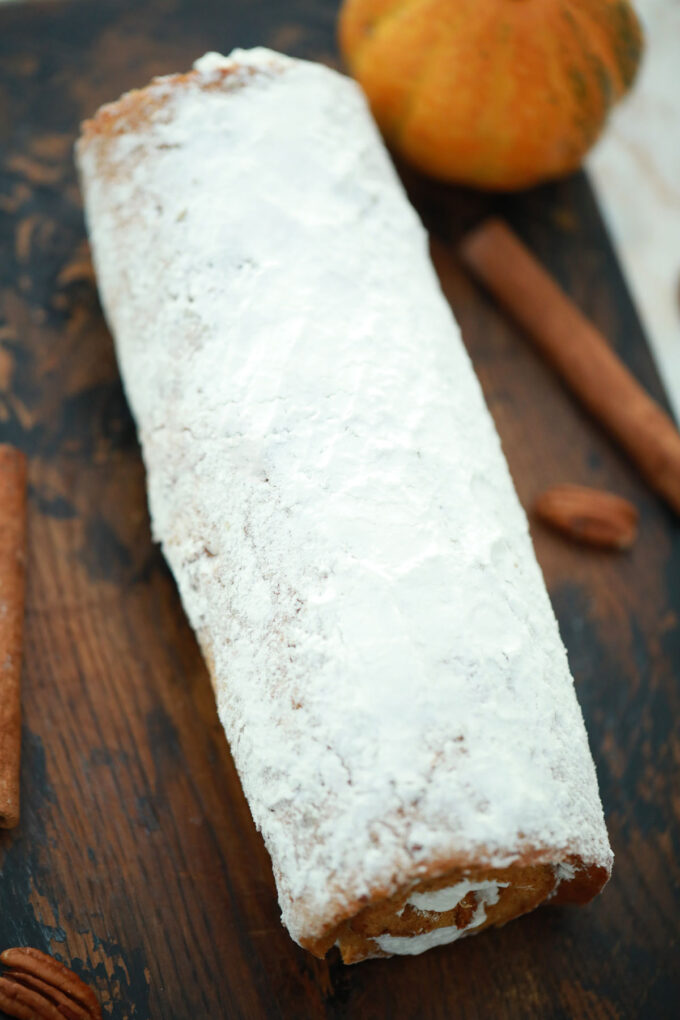 pumpkin roll with cream cheese frosting on a cutting board.