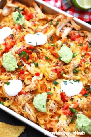 sheet pan of chicken nachos with sour cream and guacamole