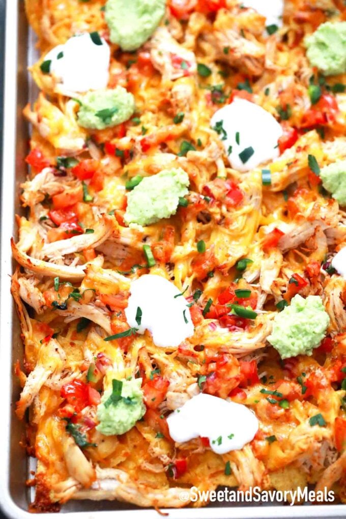 sheet pan of cheesy chicken nachos with sour cream and guacamole