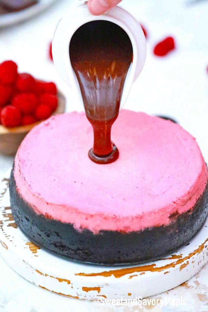 pouring chocolate ganache on top of raspberry cheesecake