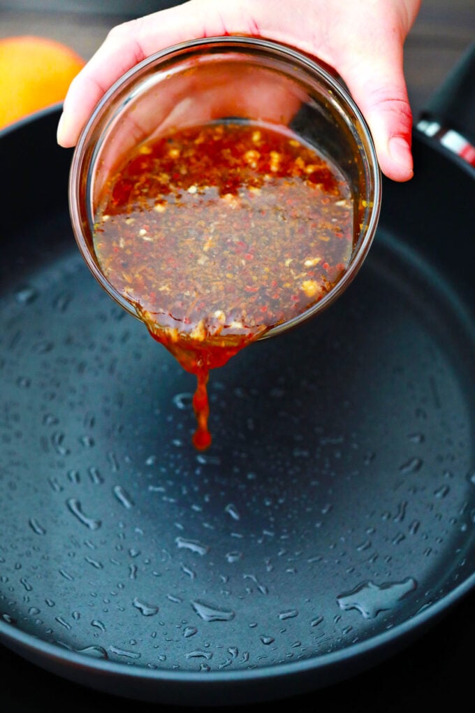 Adding homemade orange sauce to a pan.