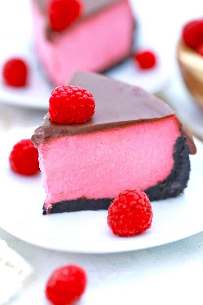 a slice of raspberry cheesecake with an oreo crus and chocolate ganache