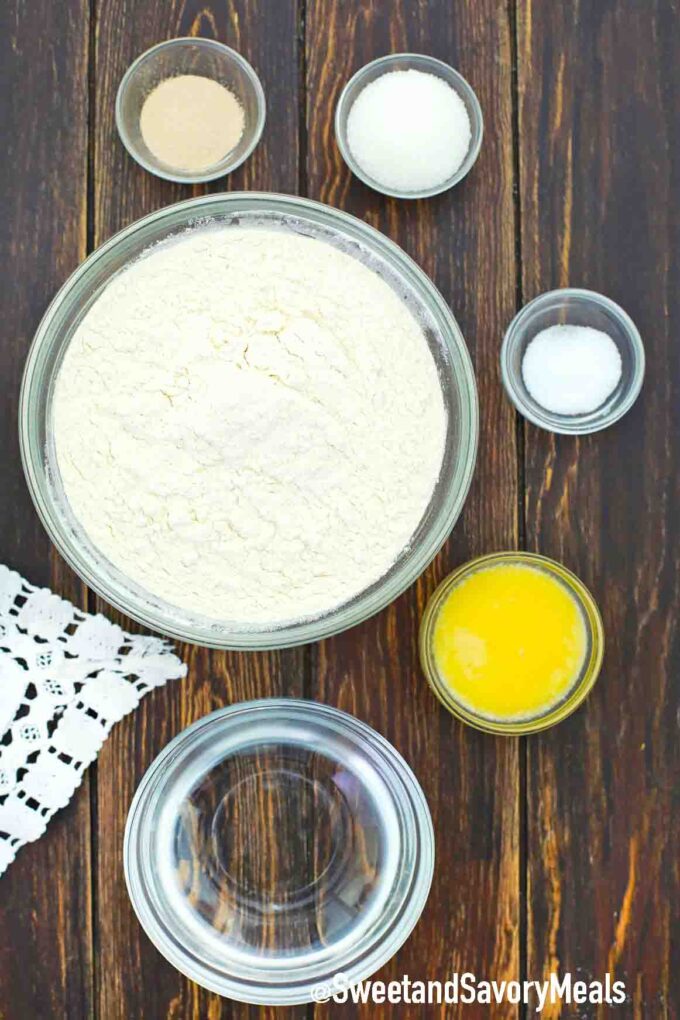 large bowl of flour and small bowls of butter water salt sugar yeast on a table