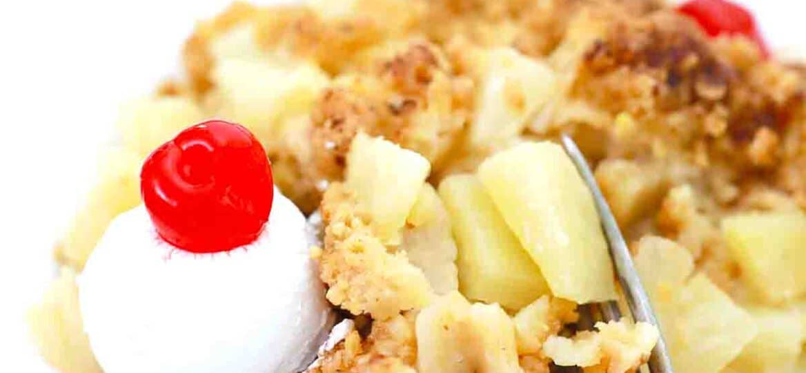 a plate of pineapple crisp with whipped cream and maraschino cherry