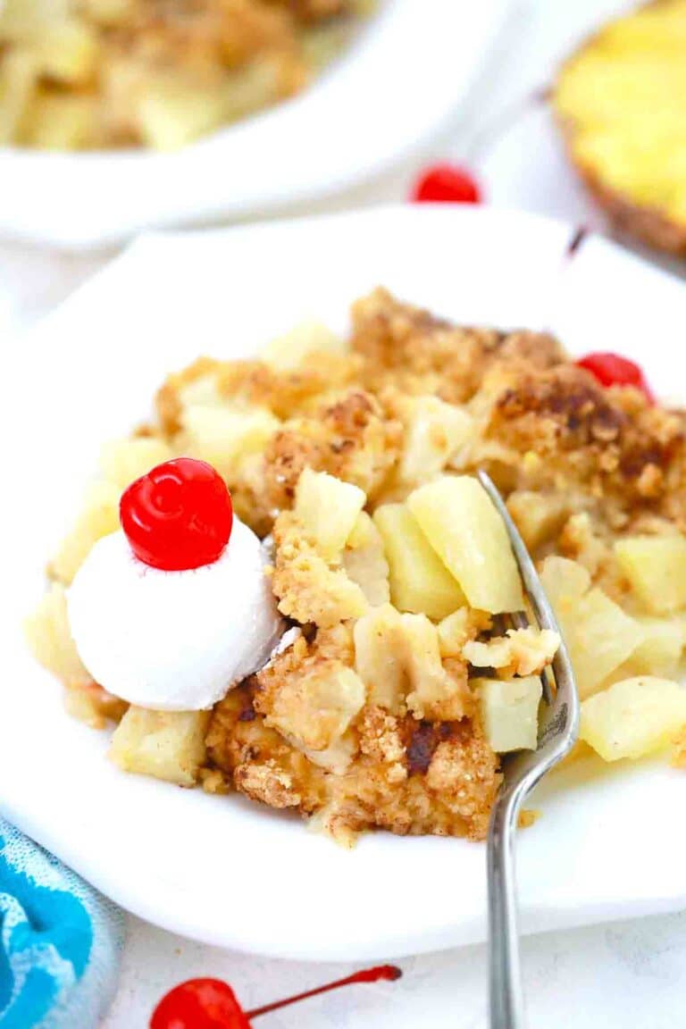 a plate of pineapple crisp with whipped cream and maraschino cherry