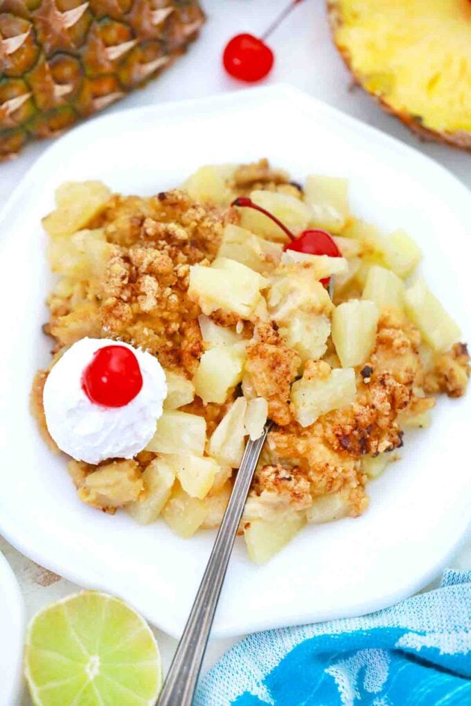 a plate of pineapple crisp with whipped cream and maraschino cherry