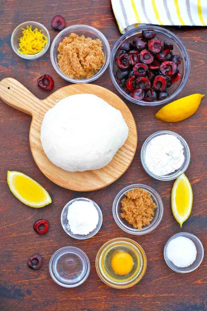 overhead shot of cherries in a bowl dough on a cutting board and other ingredients in bowls on a table