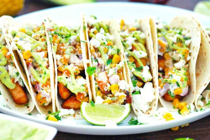 a plate of mexican street corn chicken tacos with lime wedges on the side