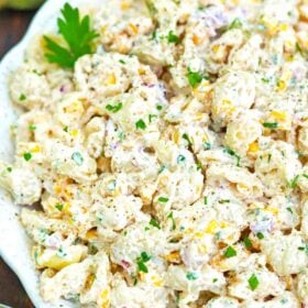 a bowl of creamy mexican street corn pasta salad with a fresh corn in the background