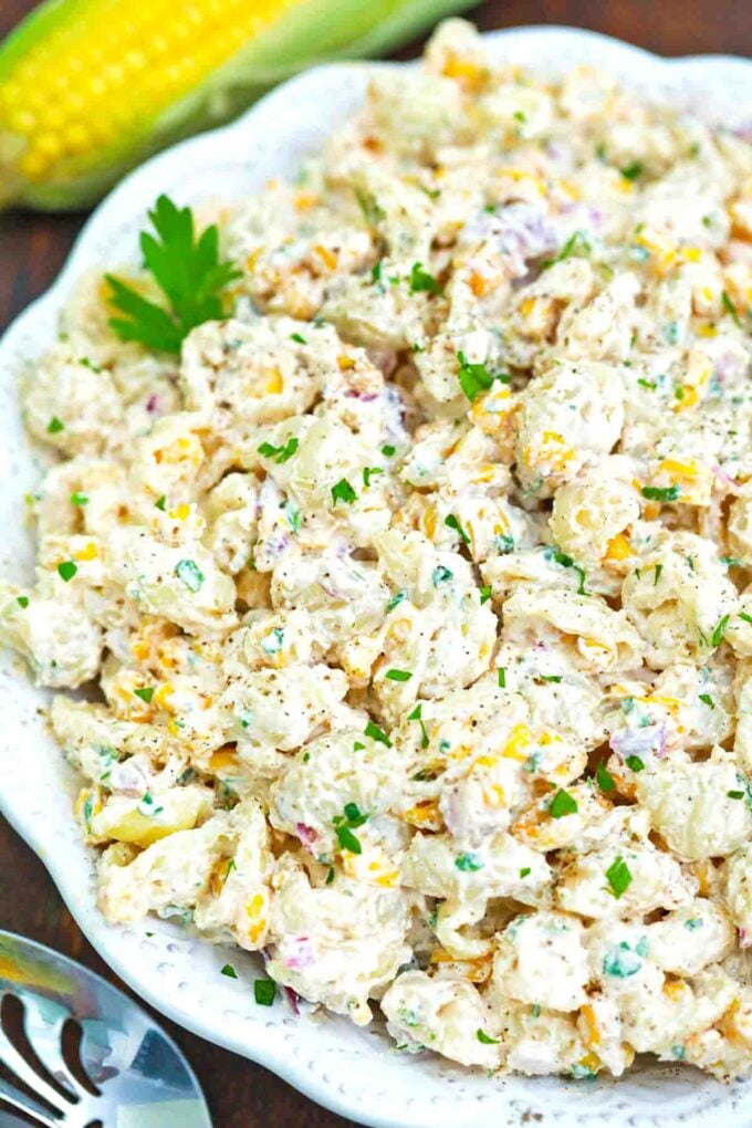 a bowl of creamy mexican street corn pasta salad with a fresh corn in the background