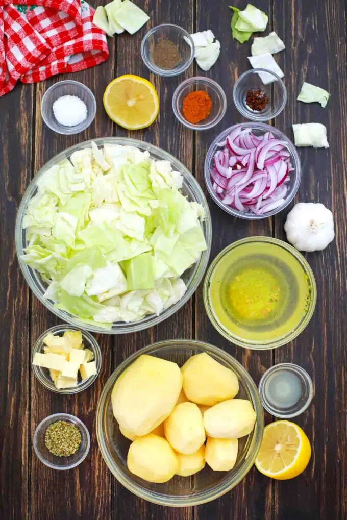 overhead shot of potatoes cabbage onion broth and spices in bowls on a wood surface