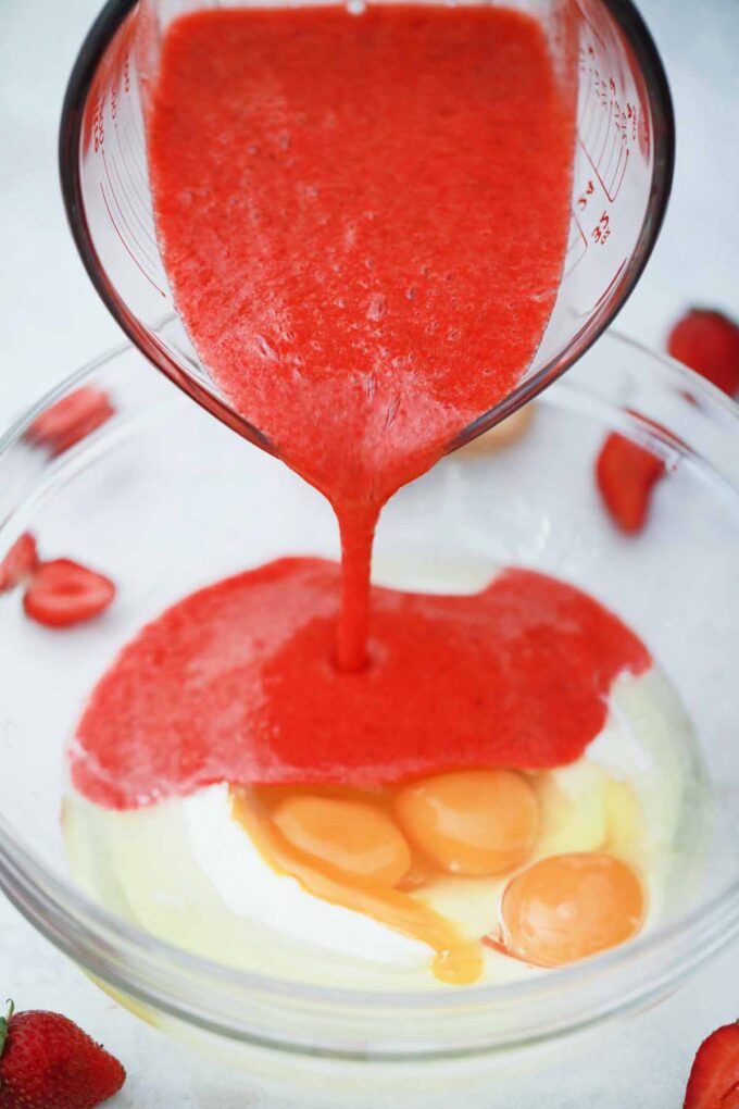 Adding strawberry sauce to eggs and sour cream in a bowl.