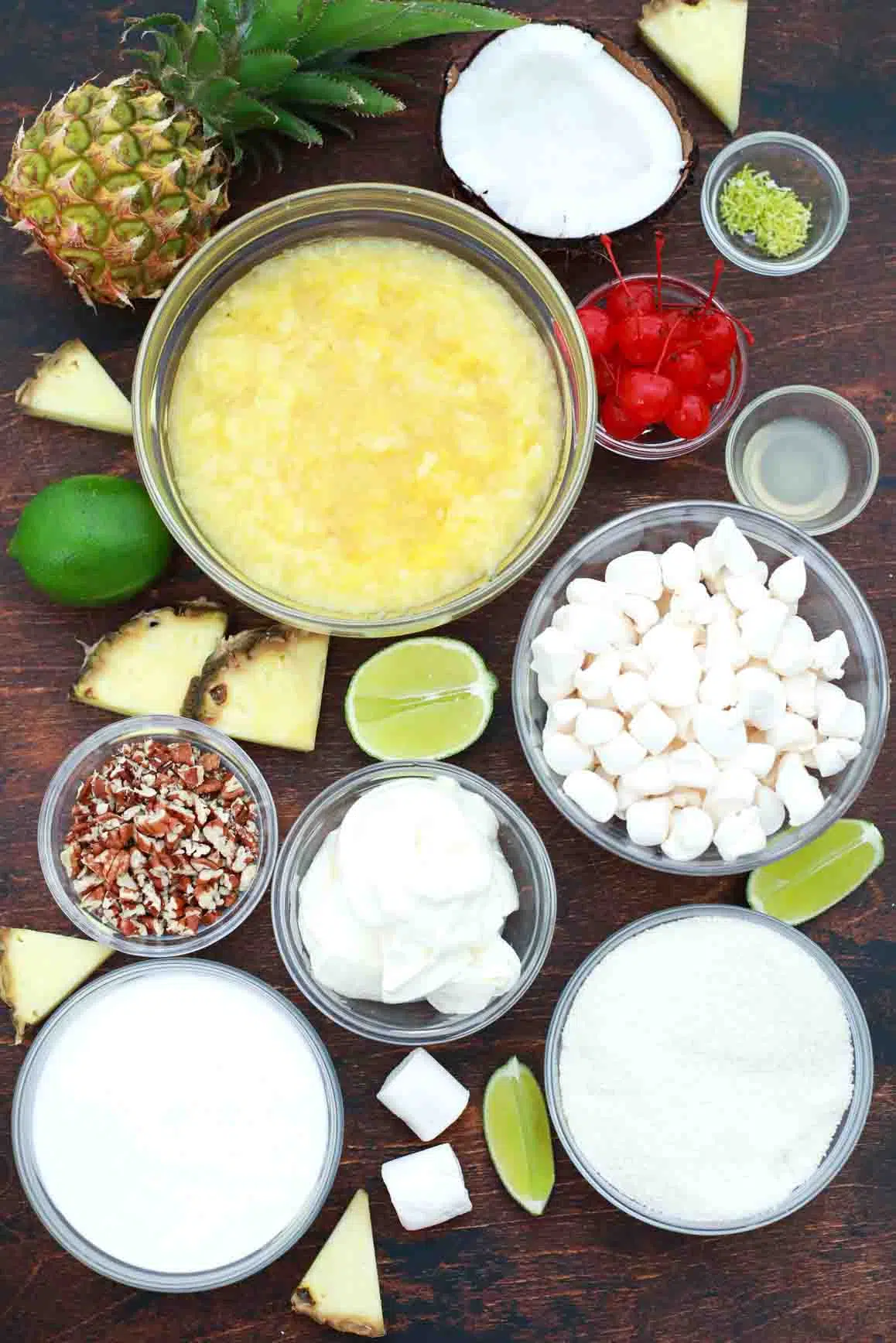 overhead shot of crushed pineapple pecans marshmallow whipped cream and pudding in bowls on a table
