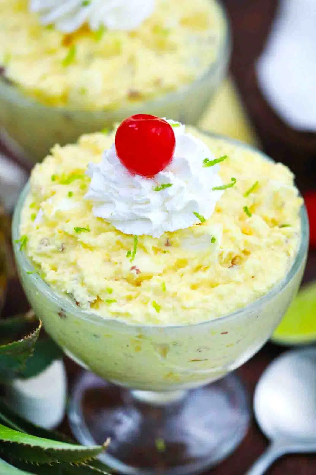 close shot of a cup of pineapple fluff topped with whipped cream and maraschino cherry