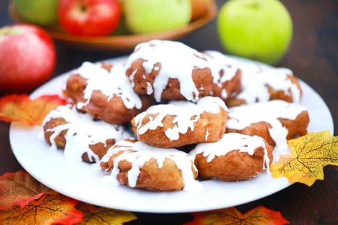 a plate of apple fritters with maple glaze and apples in background