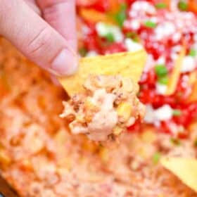 scooping creamy sausage queso dip on corn chips