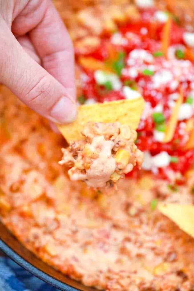 scooping creamy sausage queso dip on corn chips