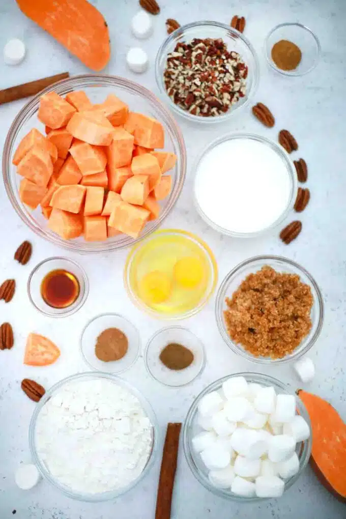 overhead shot of cubed sweet potatoes melted butter sugar spices marshmallows and pecans in bowls on a table