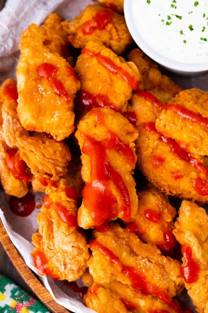 Overhead shot of crispy boneless chicken wings drizzled with hot sauce.