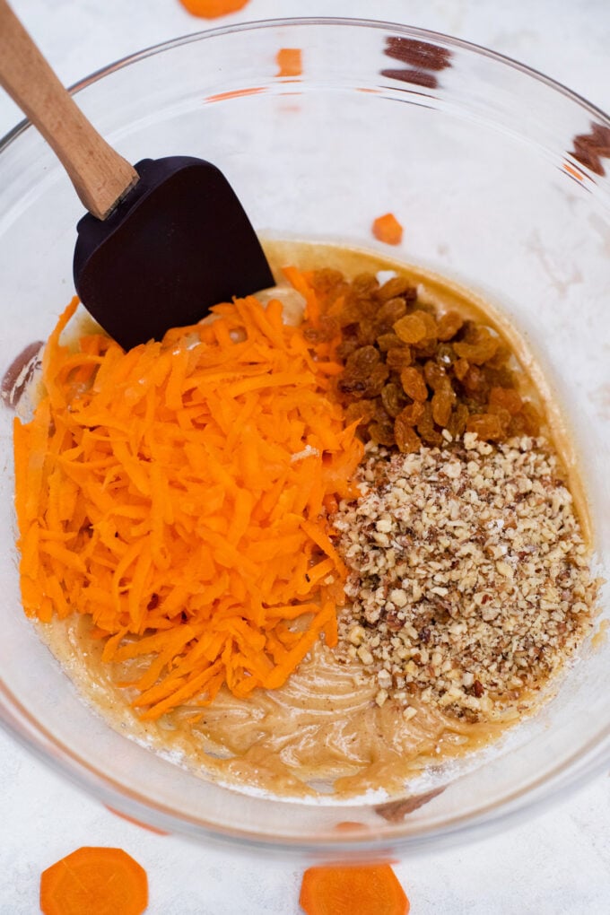 Mixing walnuts, grated carrots, and raisins into carrot cake batter.