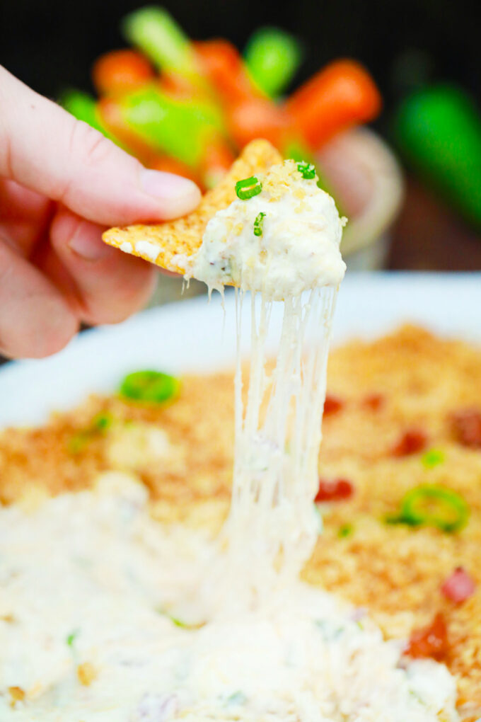 Scooping cheesy jalapeno popper dip with a corn chip.