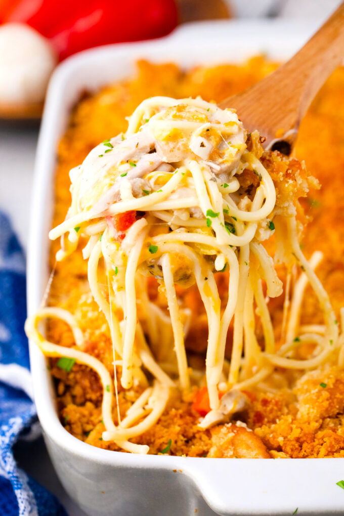 A serving spoon of baked chicken spaghetti casserole with chicken and veggies.