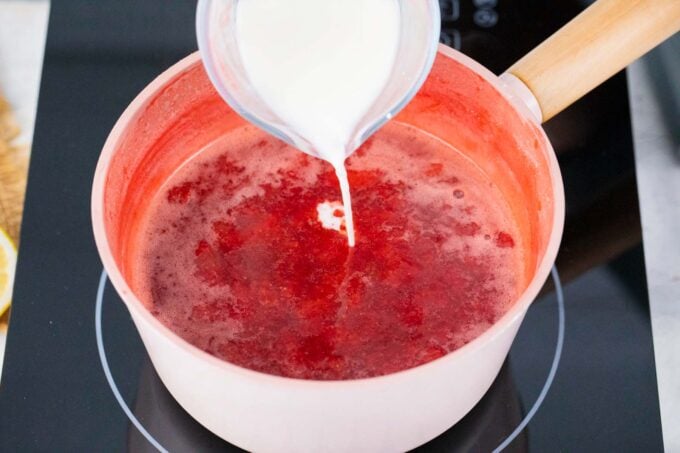 Adding cornstarch slurry to strawberry jam mixture in a saucepan.