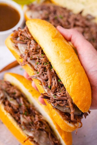 Serving tender slow cooker French dip sandwiches with cheese and shredded beef.