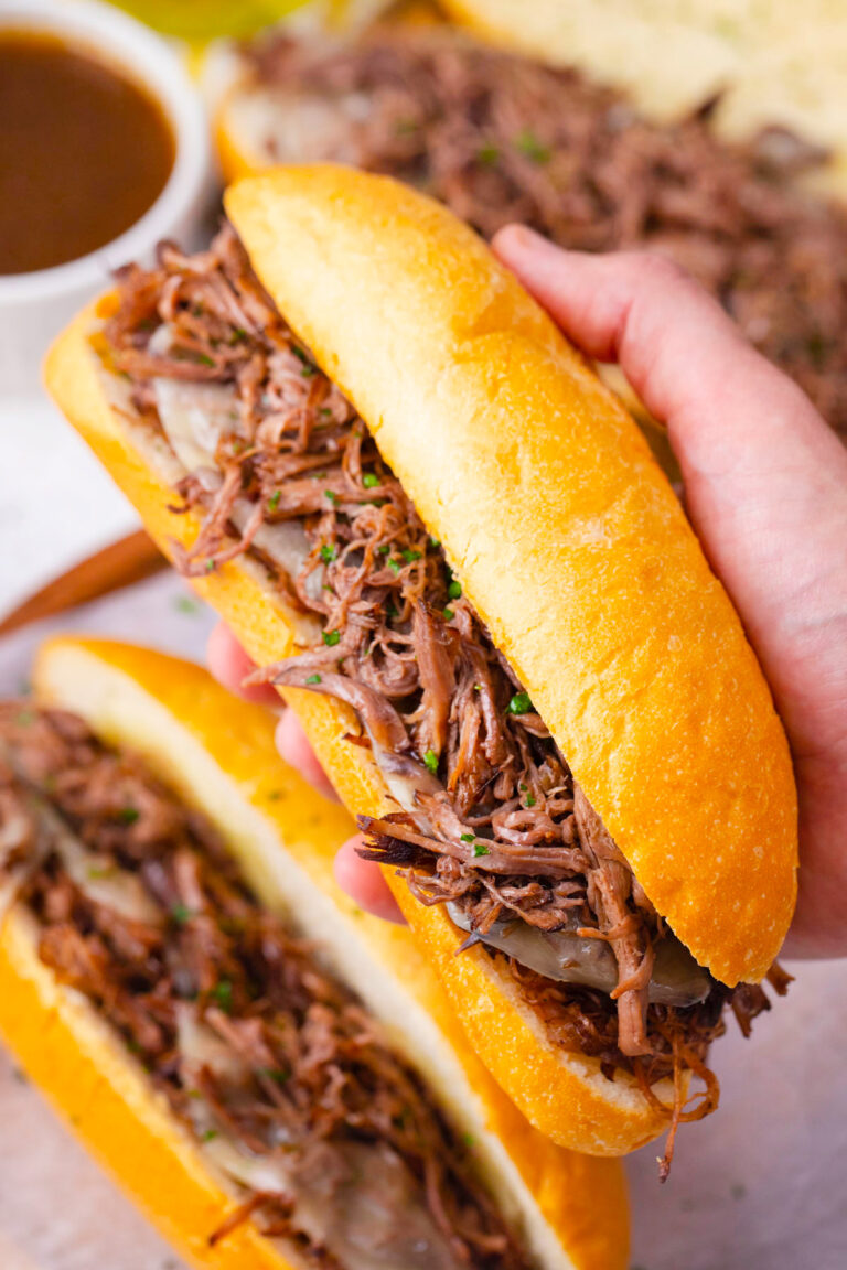 Serving tender slow cooker French dip sandwiches with cheese and shredded beef.