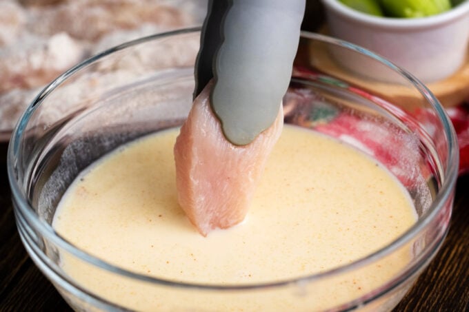 Dipping chicken piece in beaten eggs.