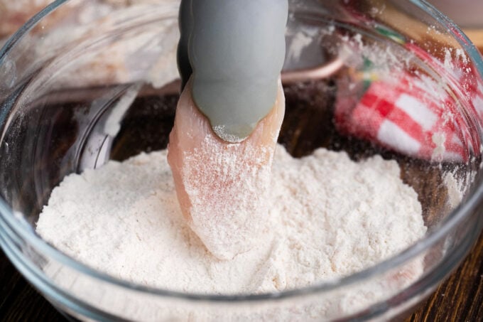 Tossing chicken piece in flour.