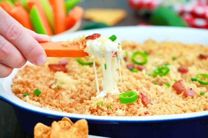 scooping jalapeno popper dip with a carrot stick