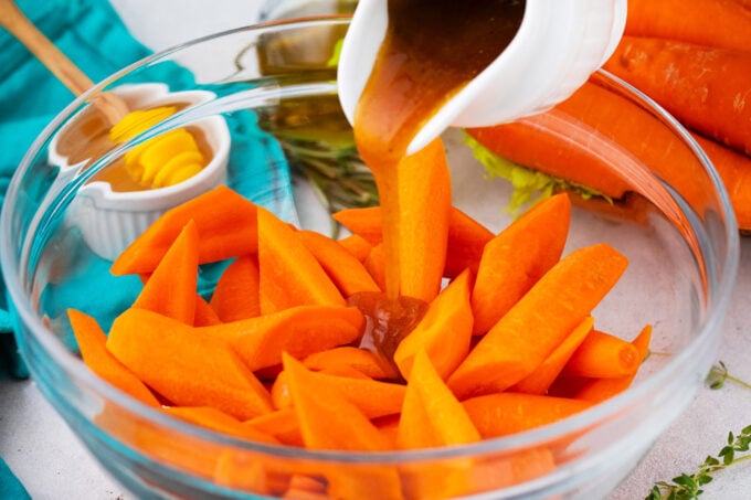 Pouring melted butter brown sugar mixture over a bowl of carrot chunks.