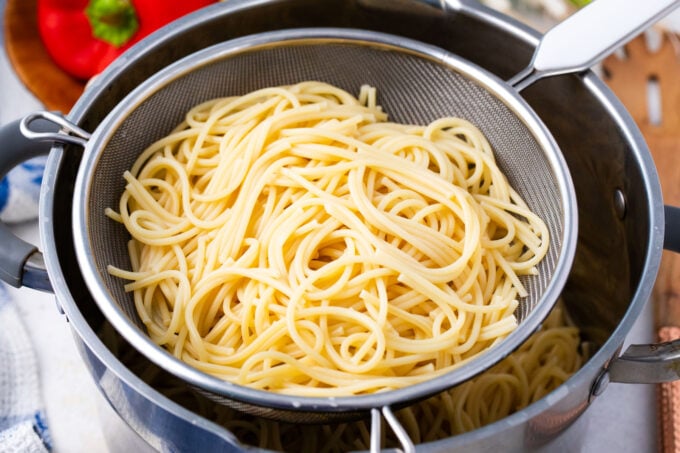 Draing spaghettini in a colander over a pot.