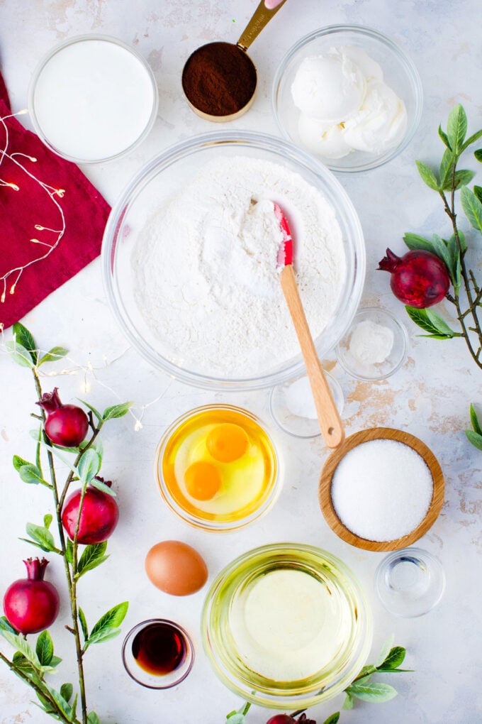 Overhead shot of red velvet cake ingredients in bowls on a light surface.