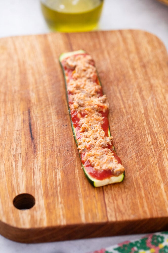 Layering ingredients on a zucchini slice to make zucchini lasagna rollups.