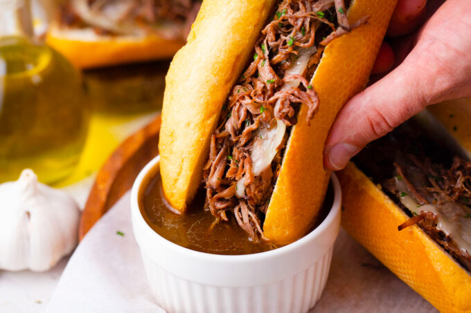 Dipping slow cooker French dip sandwich in au jus mixture.