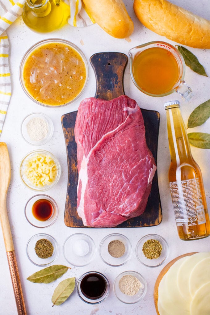 Overhead shot of slow cooker French dip sandwiches ingredients arranged on a white surface.