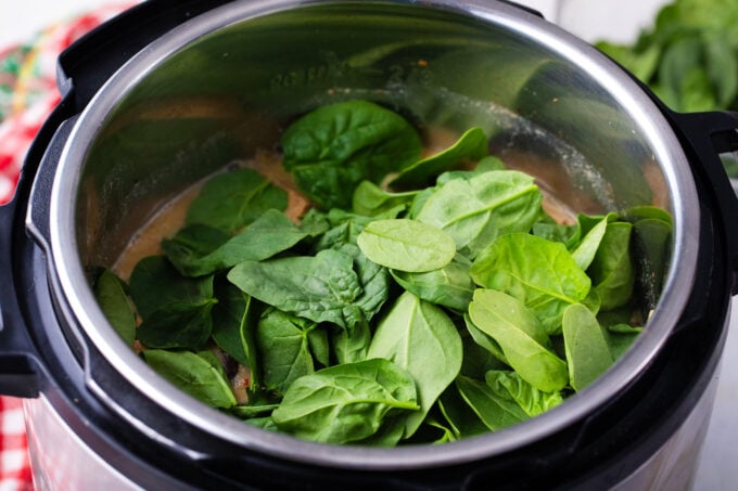 Adding spinach to Instant Pot hot and sour soup.