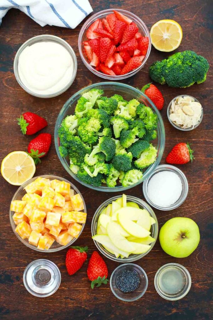 overhead shot of broccoli strawberries cheese apples mayo in bowls on a table