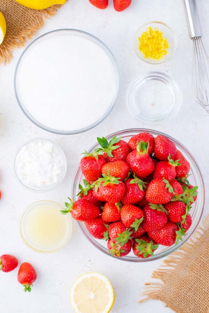 Overhead shot of strawberry jam ingredients in bowls on a table.