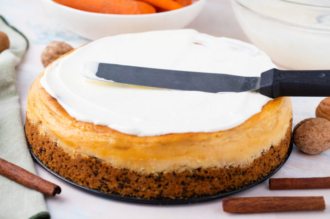 Spreading sour cream topping over carrot cake cheesecake.