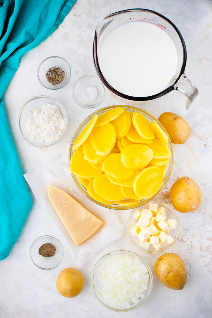 Overhead shot of bechamel sauce potato gratin ingredients in bowls on a table.