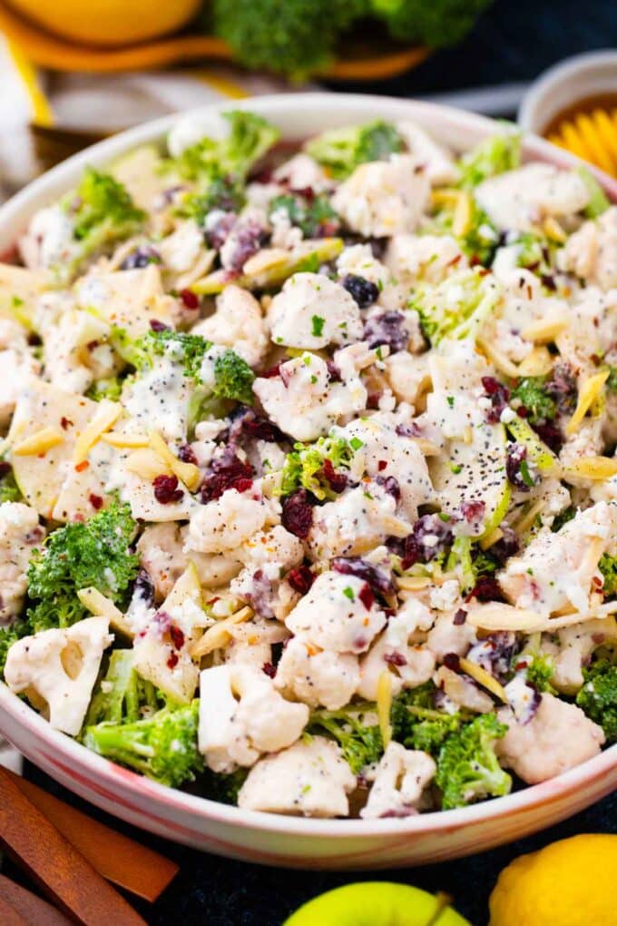 a bowl of broccoli cauliflower salad with dried cranberries and apple