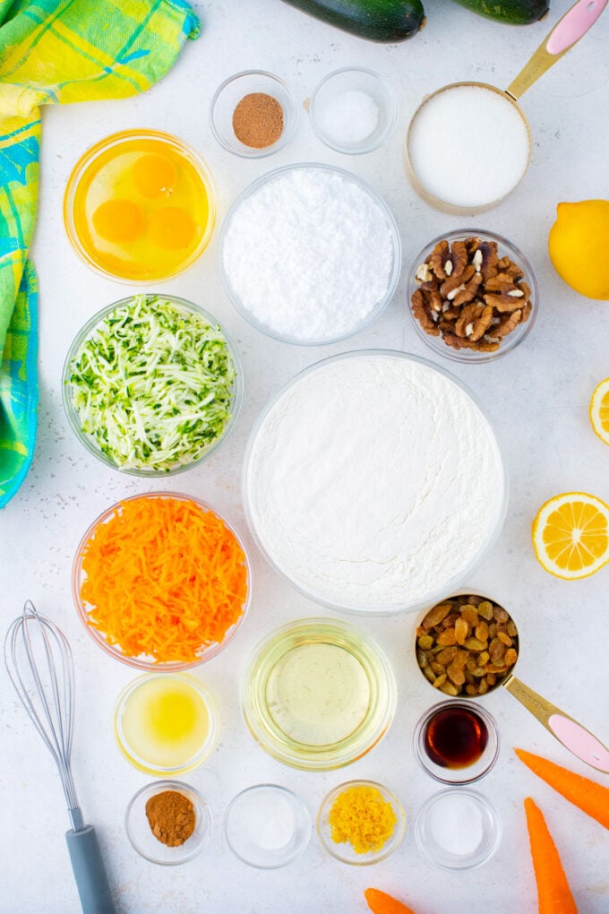 Overhead shot of carrot zucchini bread ingredients in bowls on a white surface.