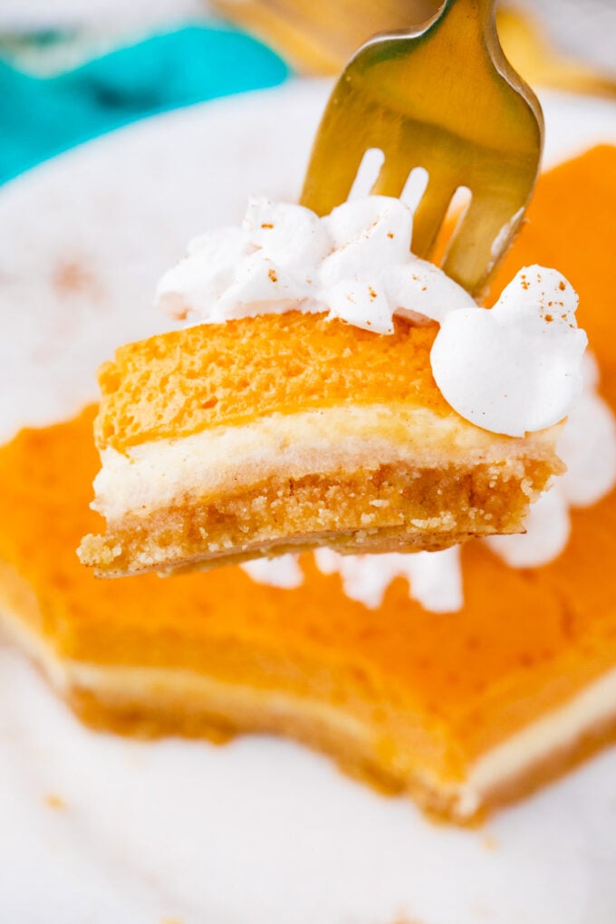 A bite of a cheesecake bar topped with whipped cream.